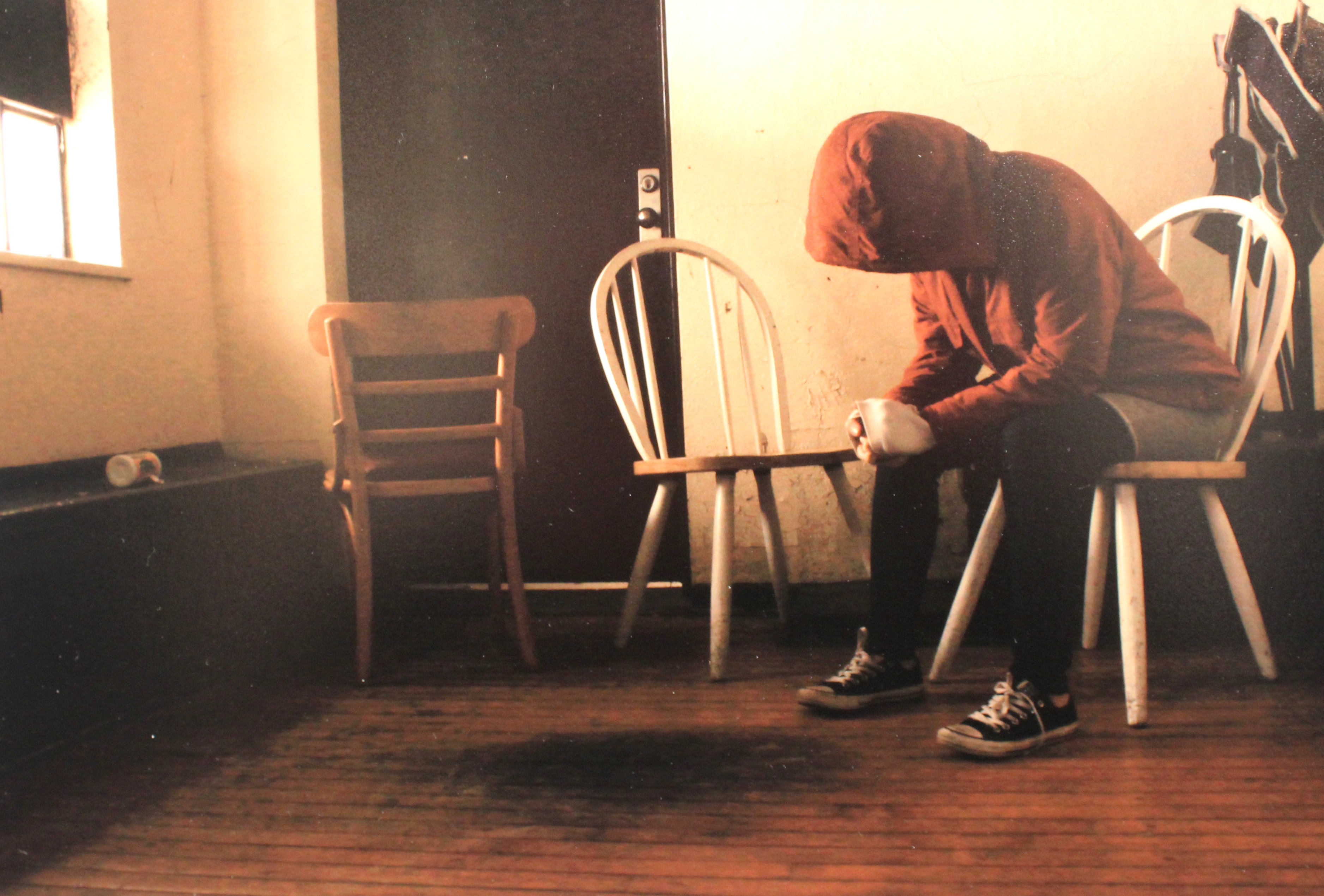 Batoul Ballout “la tete et le couer”; photo of a girl wearing a hoodie looking down at the floor where a table once stood.