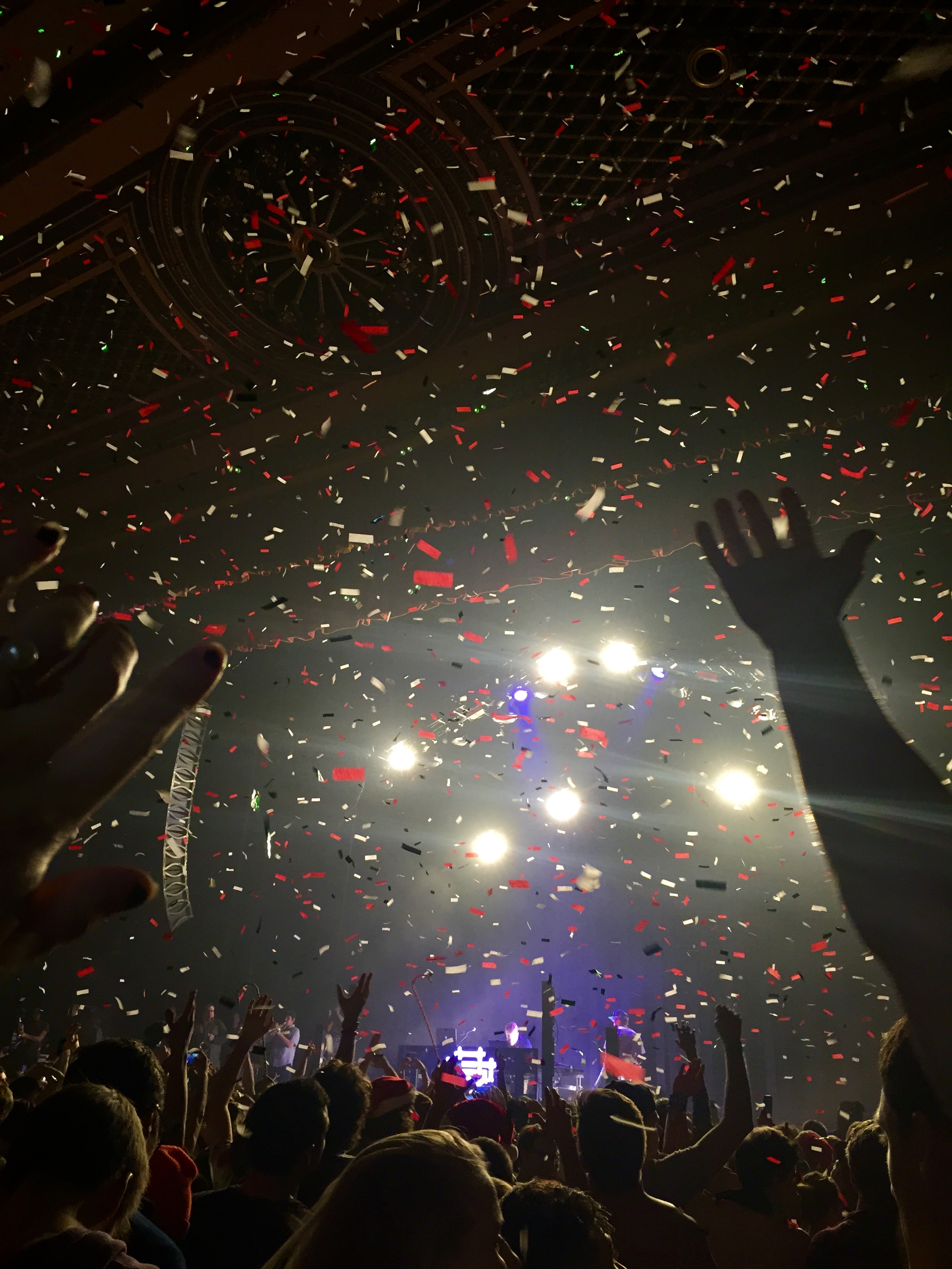 Concert photo with crowd and hands in the air and bright stage lights.