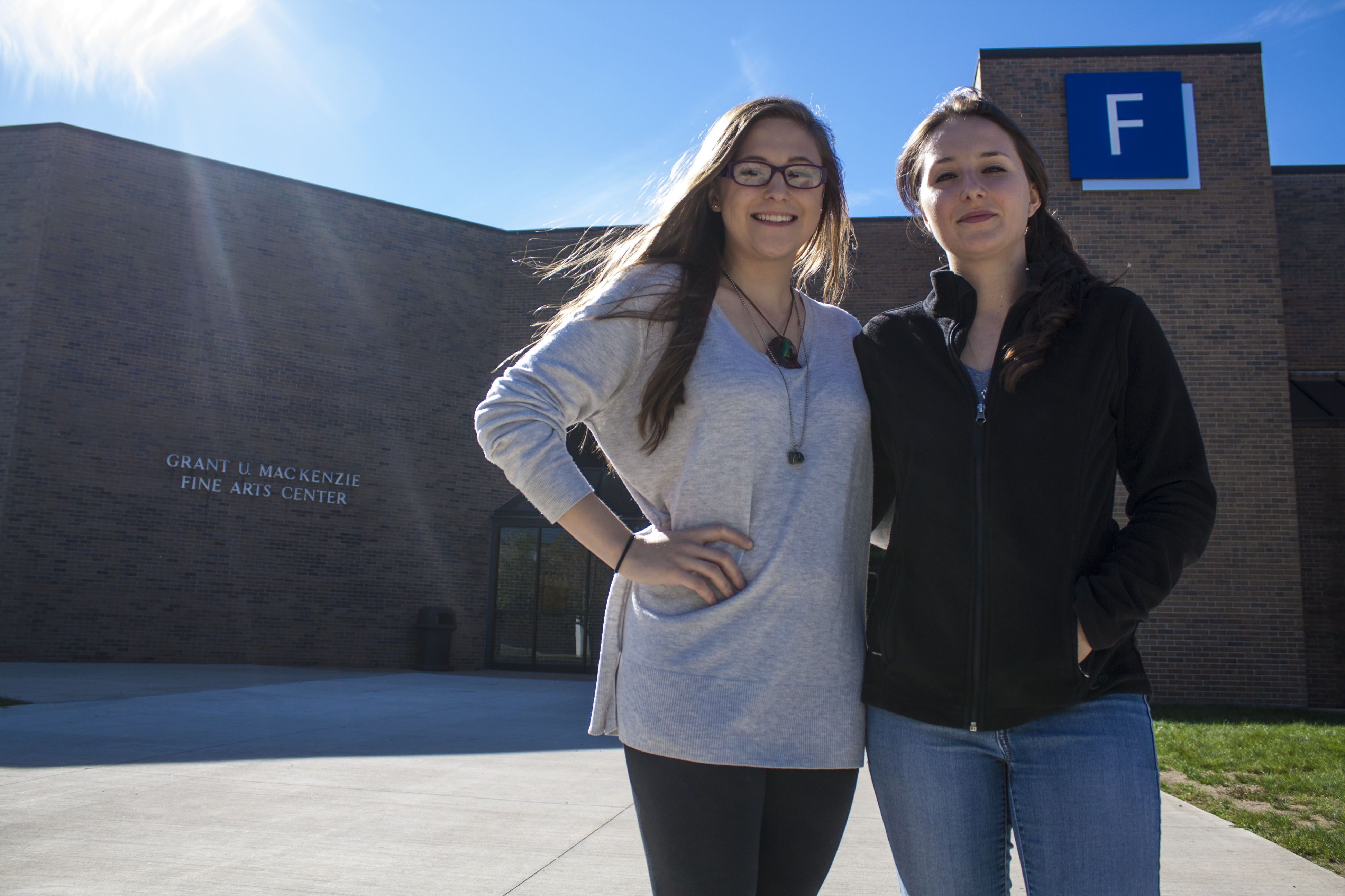 Victoria Hart and Sophia Hart standing outside the Fine Arts building at Henry Ford College in the fall with the sun shining.