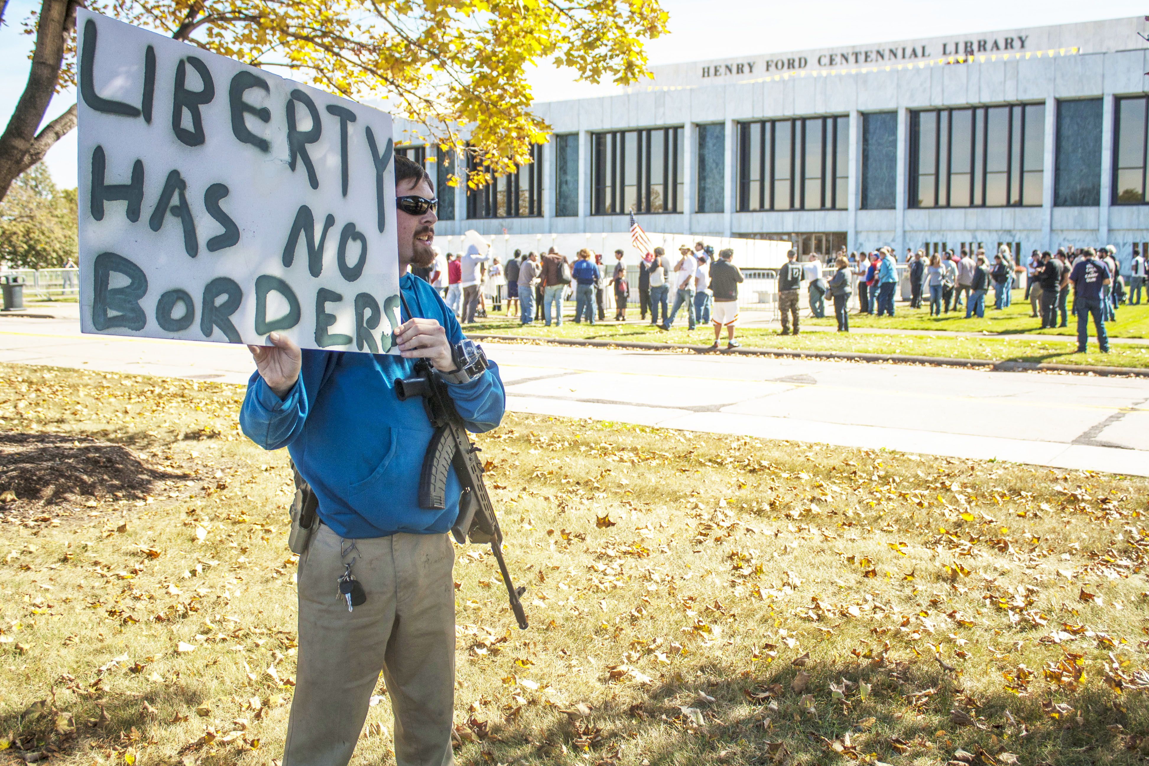 Man with assault rifle in front of Dearborn Public Library holding sign saying Liberty Has No Borders