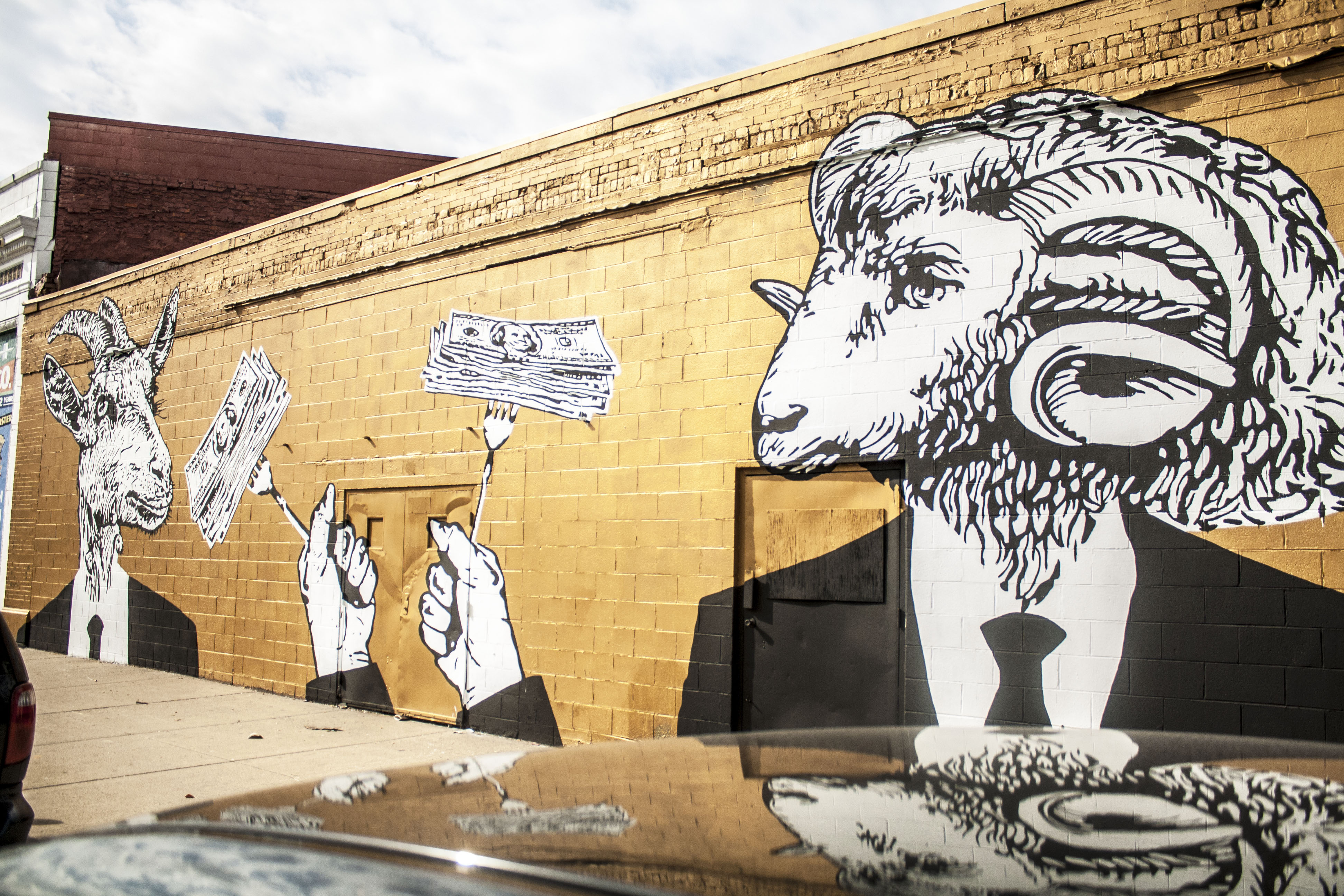 Mural of two goat people wearing black and white suit and tie holding forks spearing stack of dollar bills.