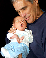 Photo of father, Brian Burke, holding his newborn baby in white and baby blue newborn clothes.