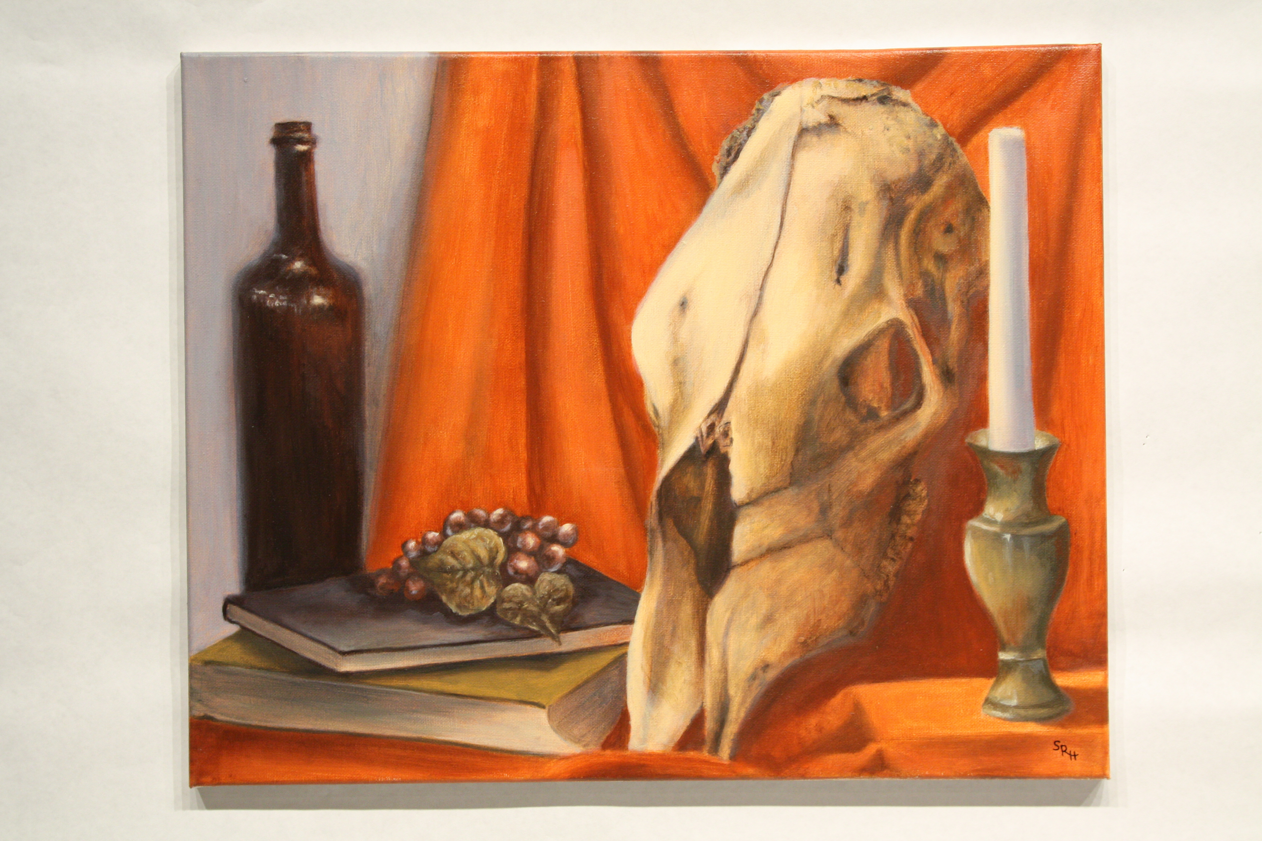 Painting of animal skull with orange drapery and candle and wine bottle.