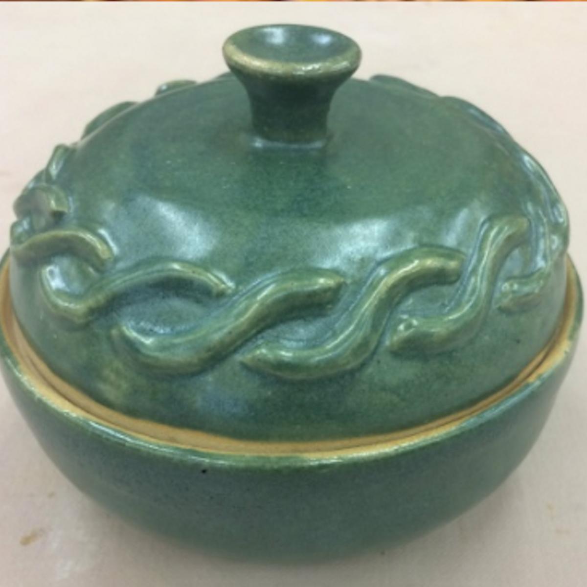 Green clay bowl and lid with Celtic weaves around the lid made by Sophia Hart.