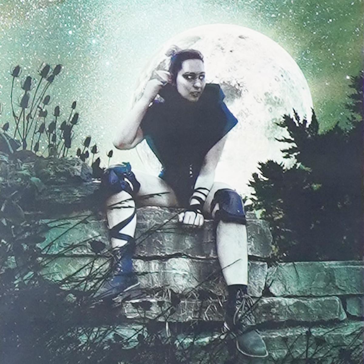 Green tinted photo of woman wearing hoodie and knee pads and boots sitting on wall with bright full moon behind her. Art by Isabelle Negron-Main